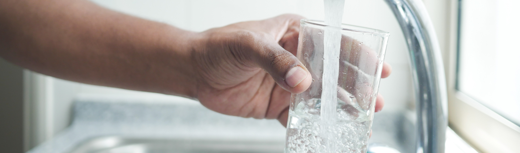person filling up glass of water at kitchen sink